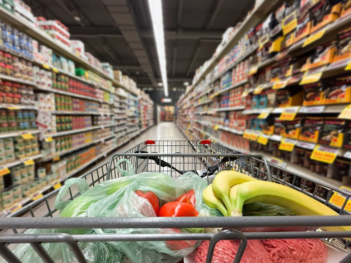 Rear view close up of shopping cart in supermarket aisle with blurred background.